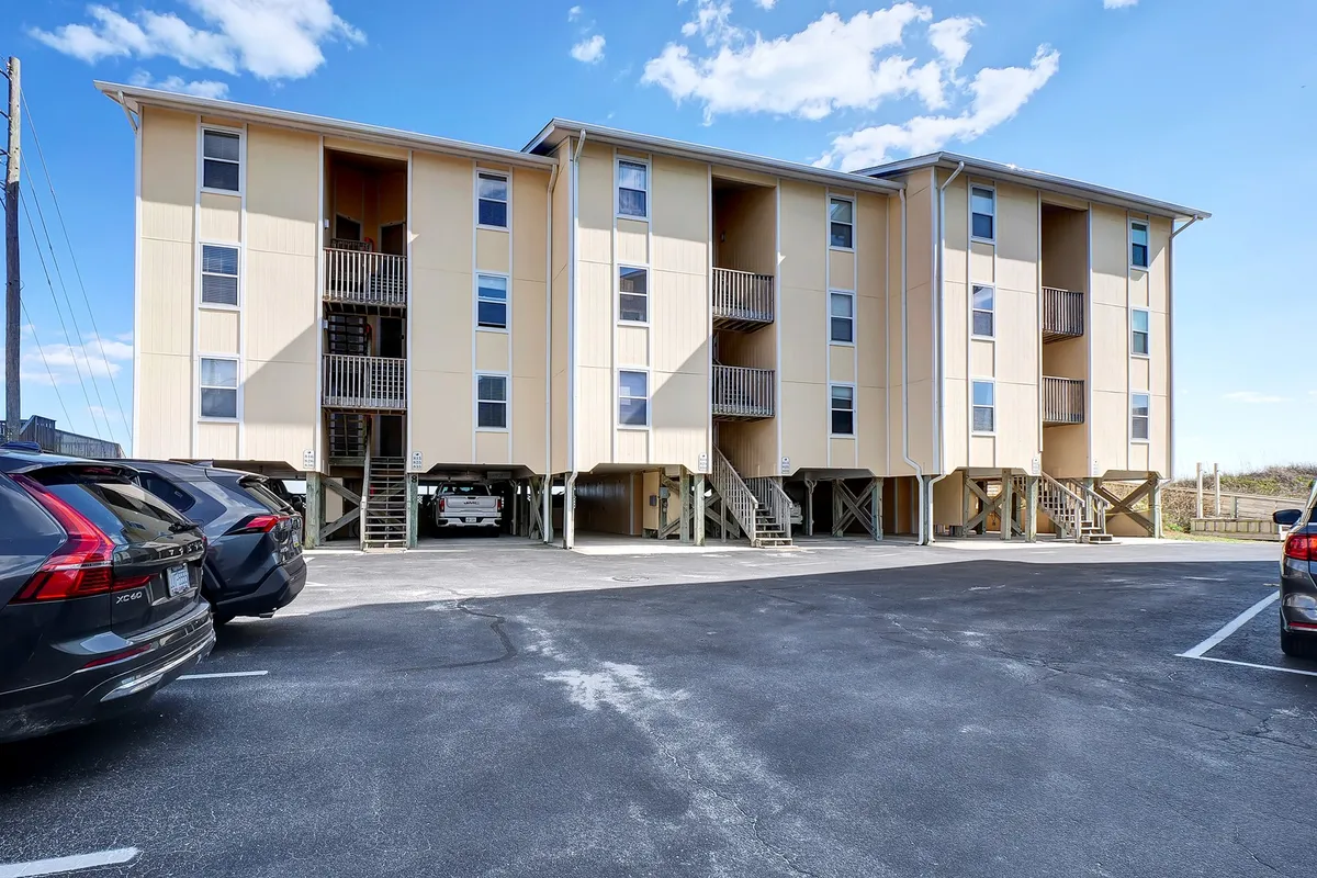 The exterior of a three-story building with balconies and a parking area. The balconies set the scene for socializing with friends or enjoying coffee outdoors, while the parking hints at easy access for exploring Surf City.