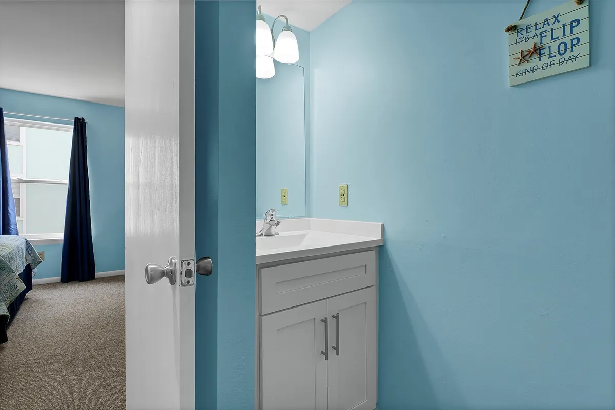 A calming bathroom scene with a modern sink, blue walls, a framed mirror, and a 'relaxing' sign. The soothing decor and efficient layout suggest a refreshing space for morning or evening routines.