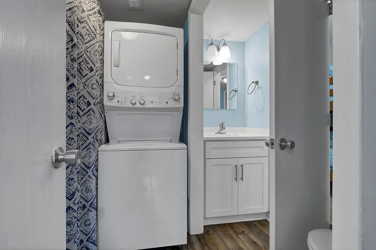 A practical laundry area with a washer and dryer unit, a vanity sink, and a mirror. The space is bright and efficient, ideal for handling laundry needs during longer stays.