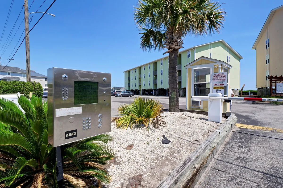 An inviting exterior shot of the property shows the building facade, palm trees, and intercom system. The outdoor space feels welcoming and hints at both security and relaxation, capturing the excitement of arrival and outdoor enjoyment.